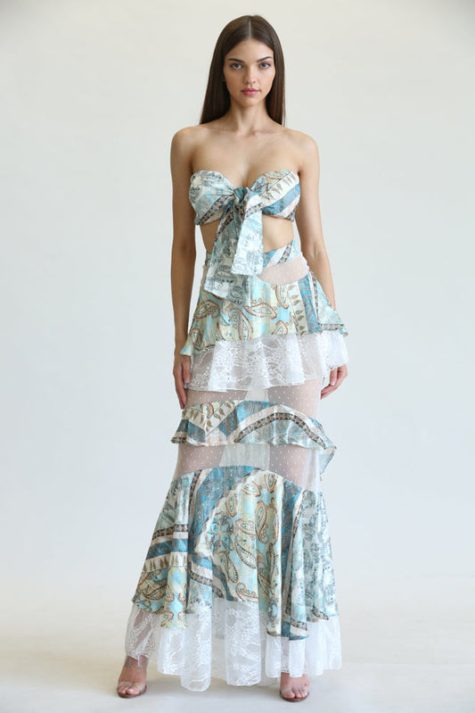 Colorful paisley-print maxi dress with ruffled tiers and a front tie detail, worn by a young woman against a white background.