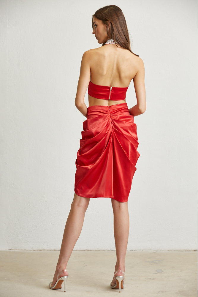 Stylish red halter top and skirt set, showcasing an elegant backless design and cinched waistline for a flattering silhouette. High-heeled sandals complete the chic, feminine look.