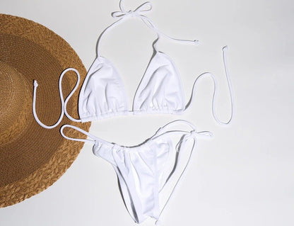 Halter neck white bikini with bow detail against a straw hat in a minimalistic studio setting