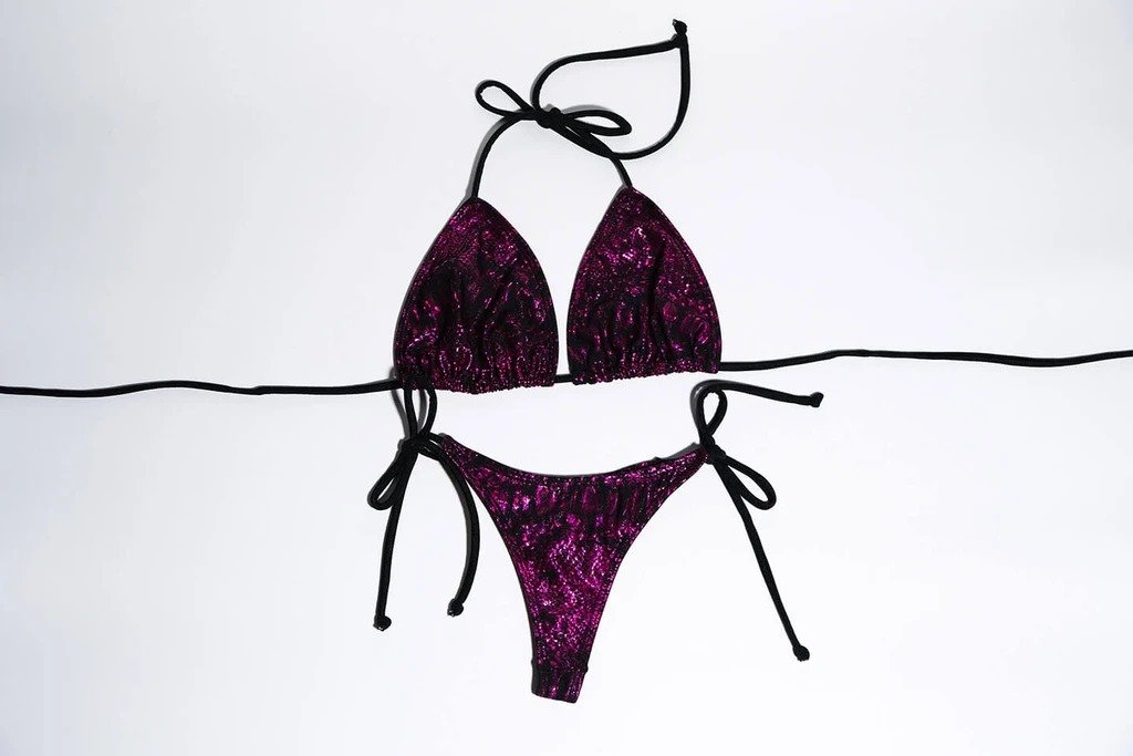 Shimmering purple bikini with spaghetti straps and tie sides, featuring an alluring floral print design against a solid white background.