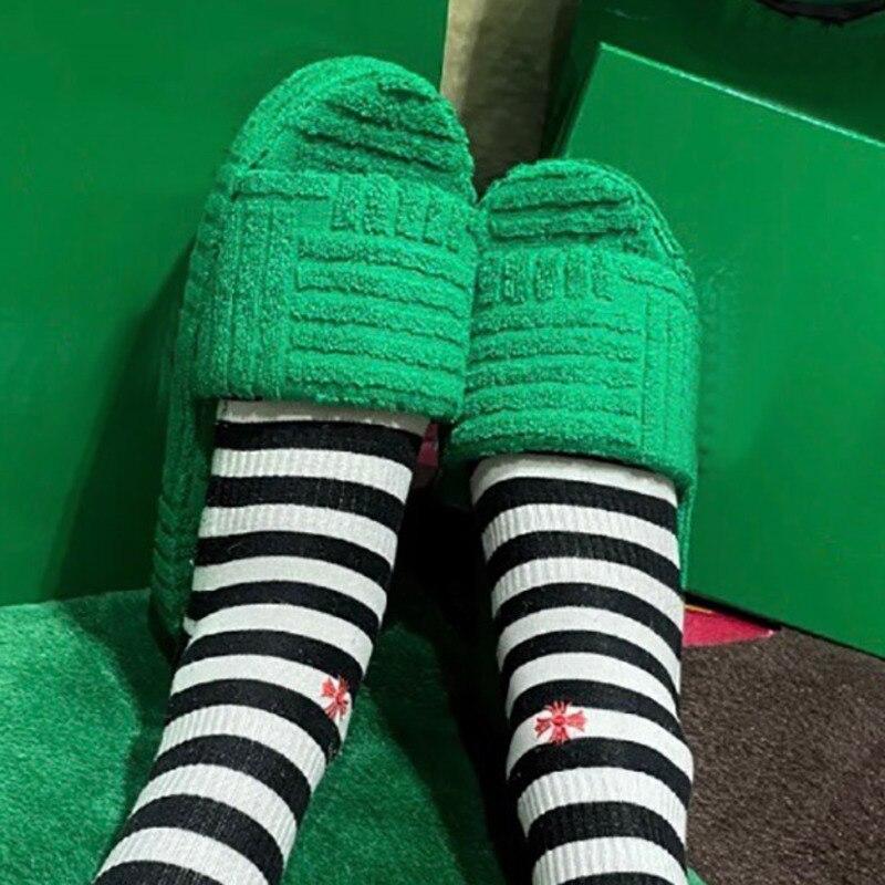 Plush green furry slippers with comfortable striped socks against a solid green background