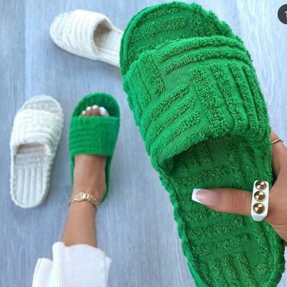 Cozy green furry slippers on a wooden floor. The plush, textured slippers have a comfortable, relaxed appearance, inviting the wearer to slip into a state of leisure and relaxation. The vibrant green color adds a fresh, natural touch to the image, complementing the neutral wood tones in the background.