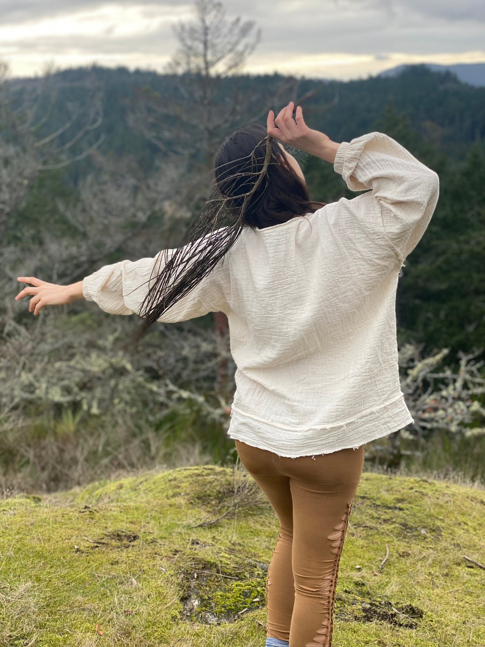 Relaxed woman in white organic cotton sweatshirt standing in natural landscape