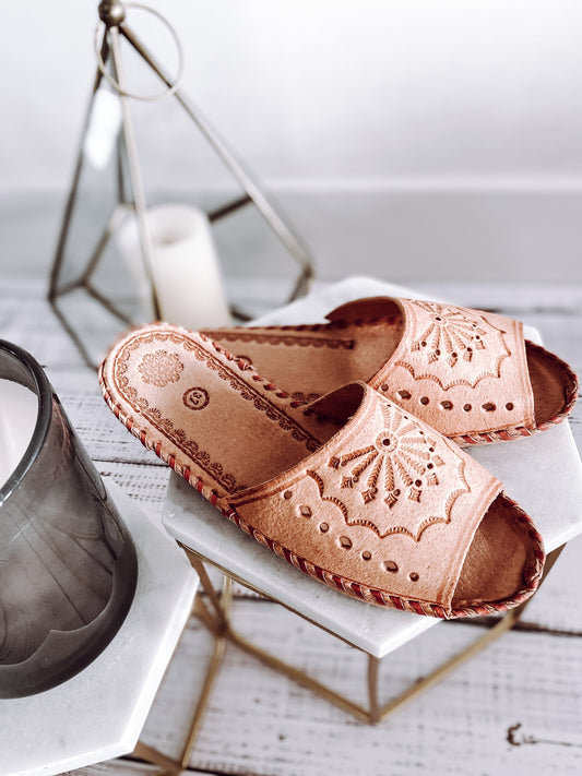 Embroidered leather slippers with intricate floral patterns on a white background with a glass vase