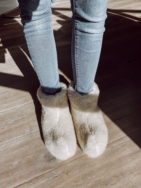 Furry white slippers on feet with denim jeans