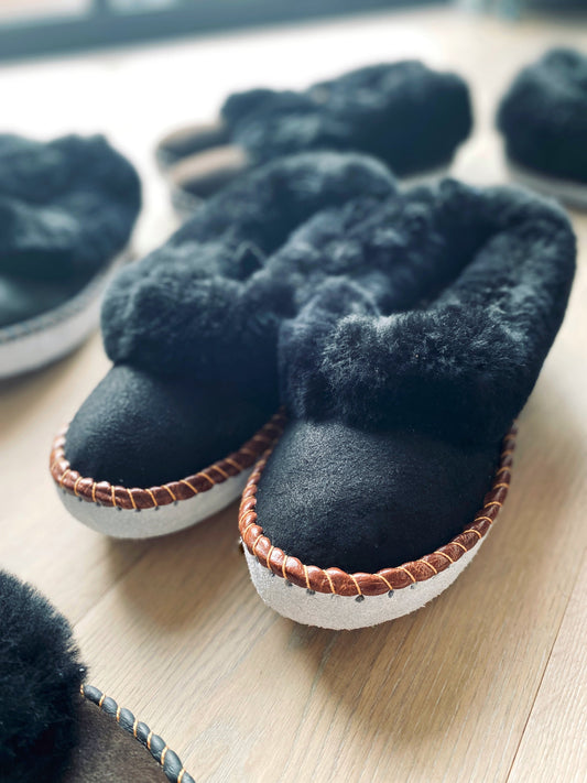 Plush black sheepskin slippers with cozy lining and textured soles on a wooden surface