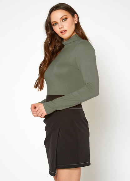 Olive green turtleneck top featuring a slim, fitted silhouette and worn by a young woman with long, wavy brown hair.