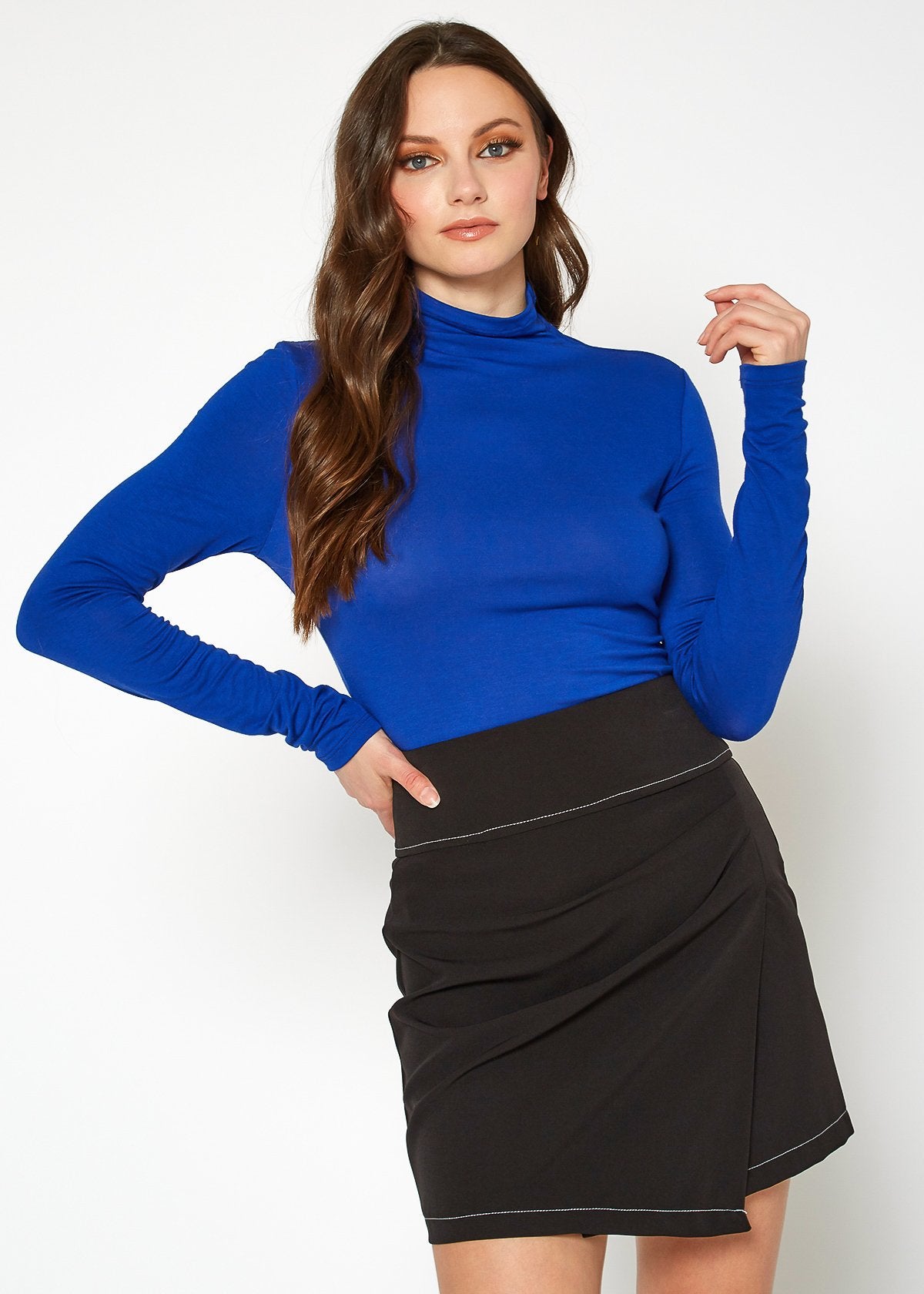 Close-up image of a woman wearing a blue long-sleeve fitted turtleneck top posing against a plain white background.