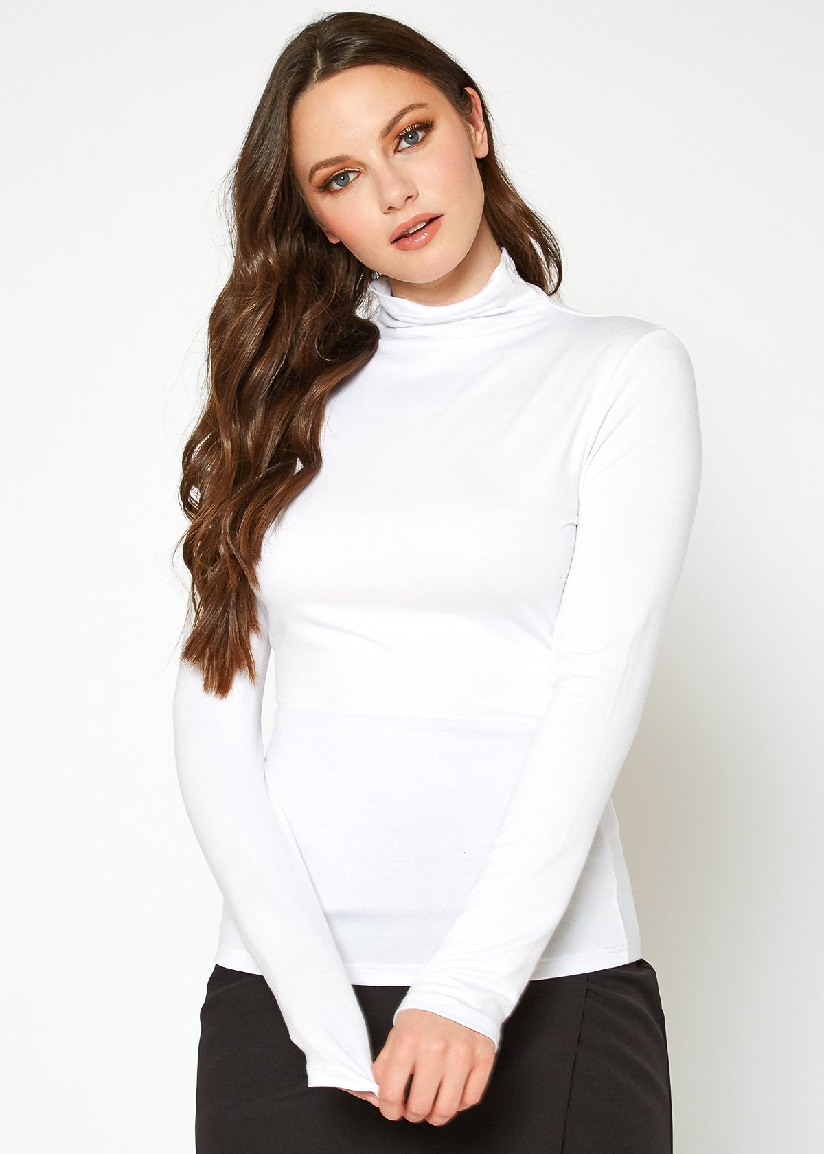 Fitted white turtleneck top with long sleeves worn by a young woman with long wavy brown hair in a plain studio setting.