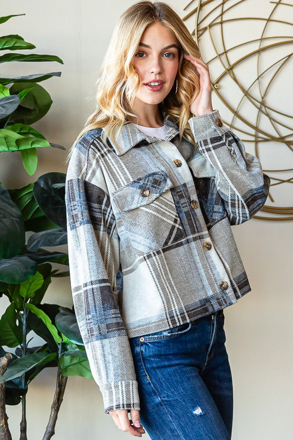 Cozy plaid button-up shacket with long sleeves, worn by a smiling blonde woman in a casual setting with lush greenery in the background