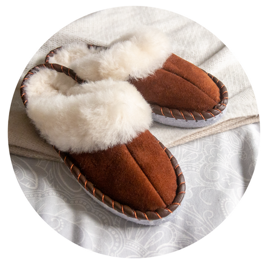 Cozy brown shearling sheepskin mules with soft fluffy lining on a patterned fabric background.