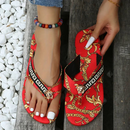 Vibrant floral print slippers with decorative chains on a white pebble background