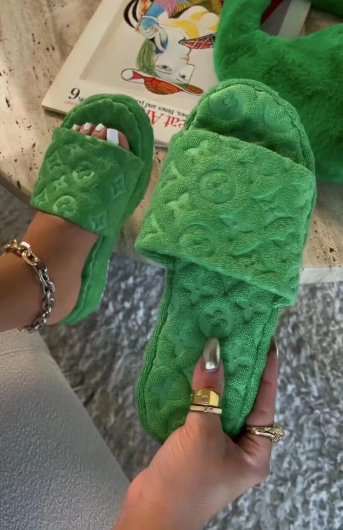 Vibrant green fuzzy slippers with flower designs, held in the hands of the wearer against a colorful background.