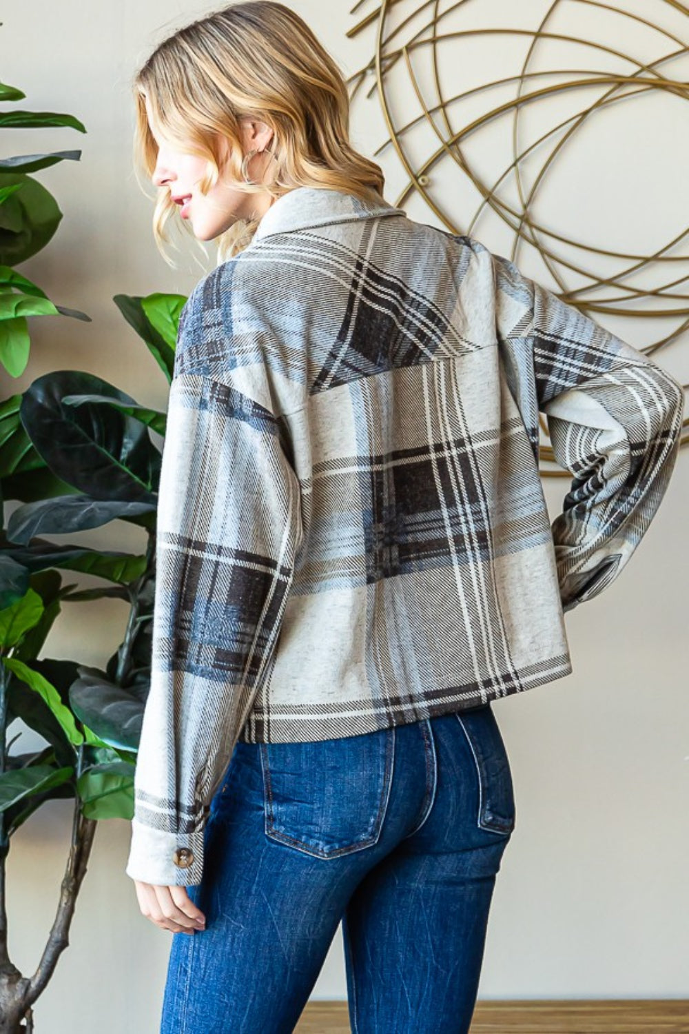 Plaid button-up shacket in grey and white tones, worn with blue jeans, displayed in a natural setting with indoor plants.