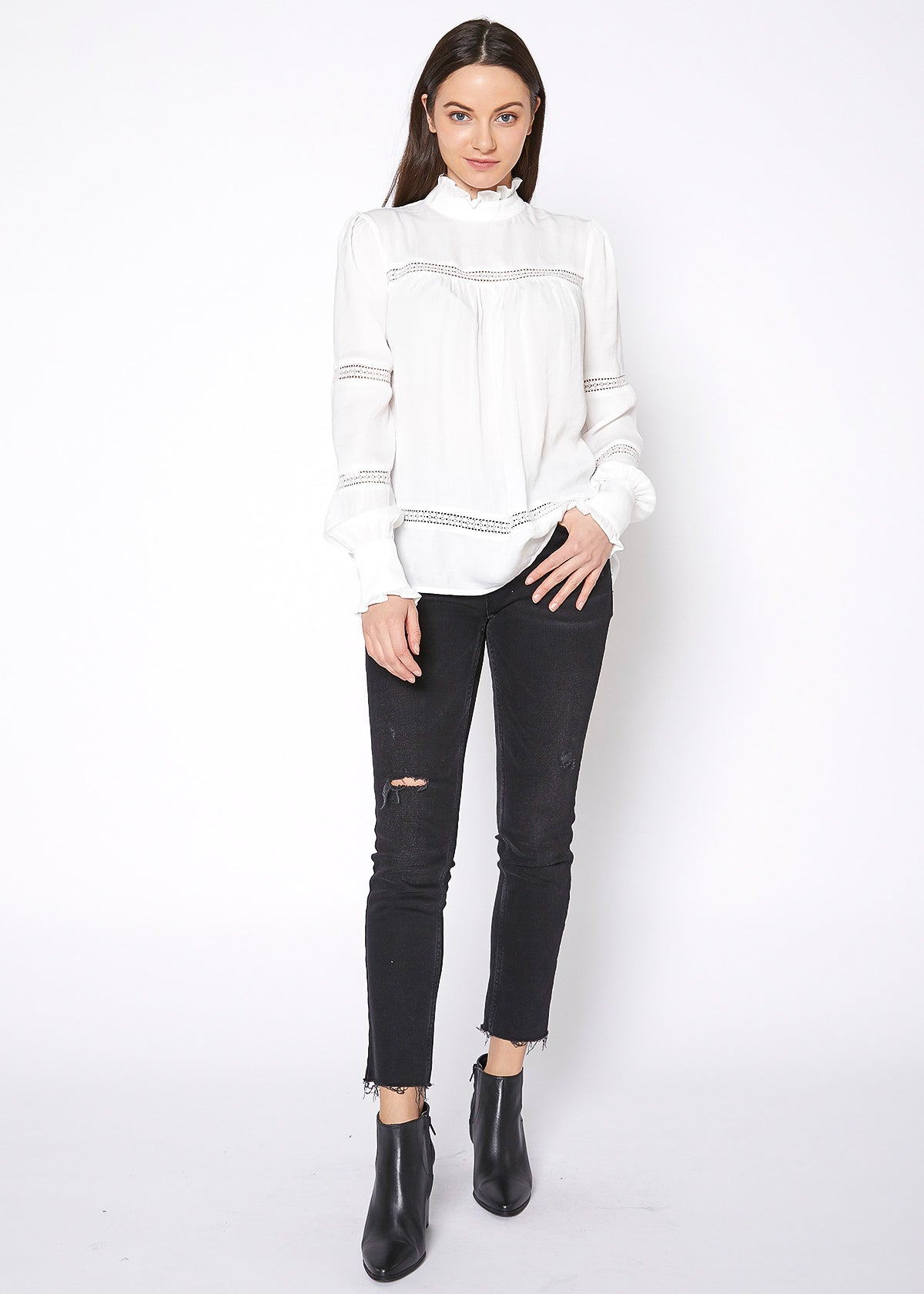 Elegant white mock-neck top with intricate eyelet details, paired with black skinny jeans for a chic, sophisticated look.