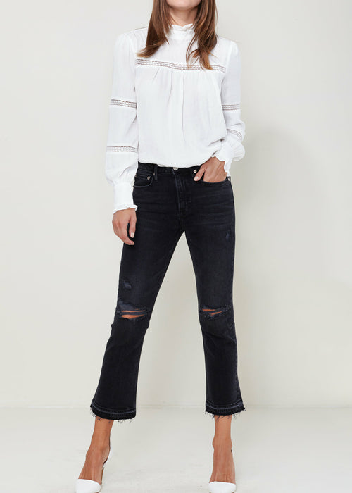 Women's mock neck blouse with eyelet details and long sleeves, paired with black cropped ripped jeans, photographed against a plain white background.