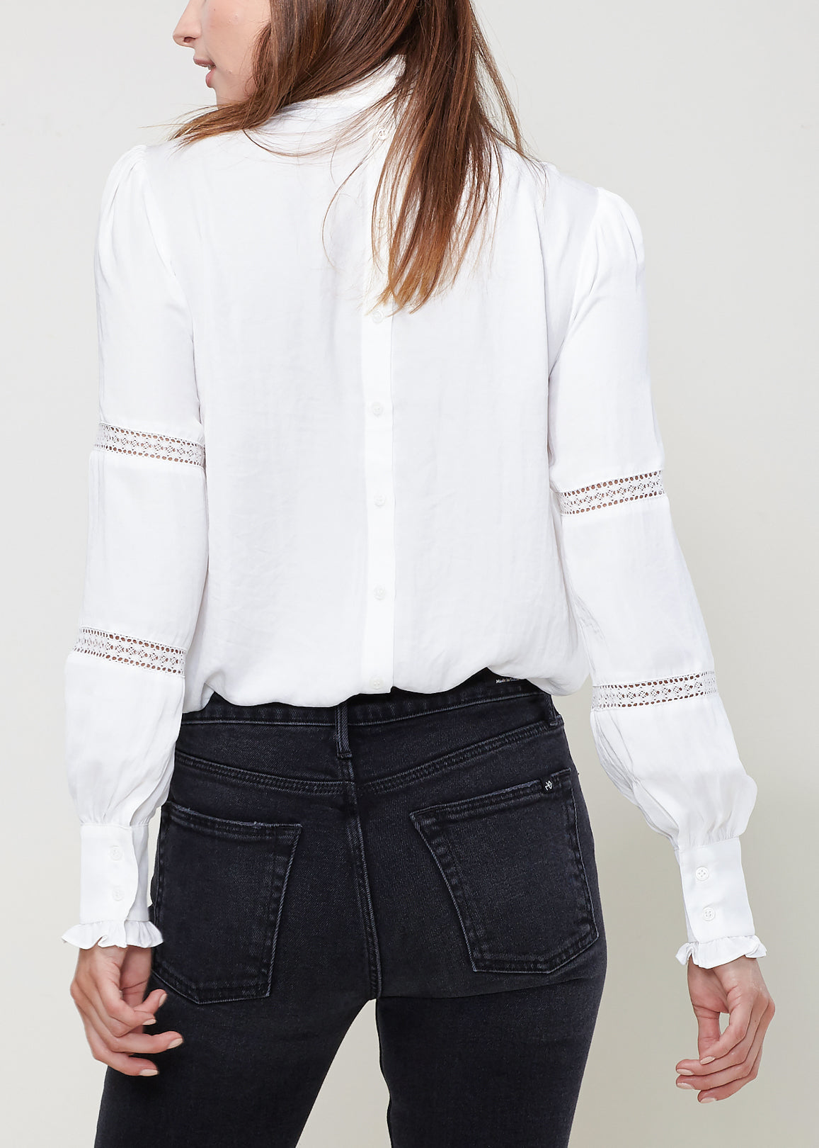 Elegant white mock neck top with eyelet details on the sleeves, worn by a female model against a plain background.