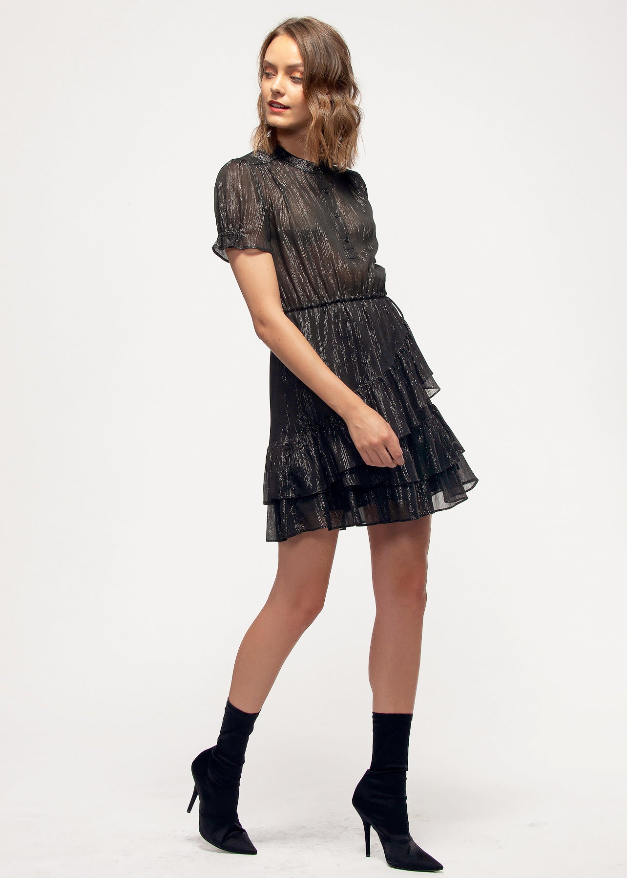 Elegant black mini dress with ruffle detailing and short puff sleeves, modeled by a young woman with wavy brown hair.