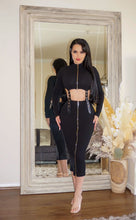 Load image into Gallery viewer, A woman wearing a sleek, black fitted dress with zipper details, posing confidently in front of a large framed mirror.