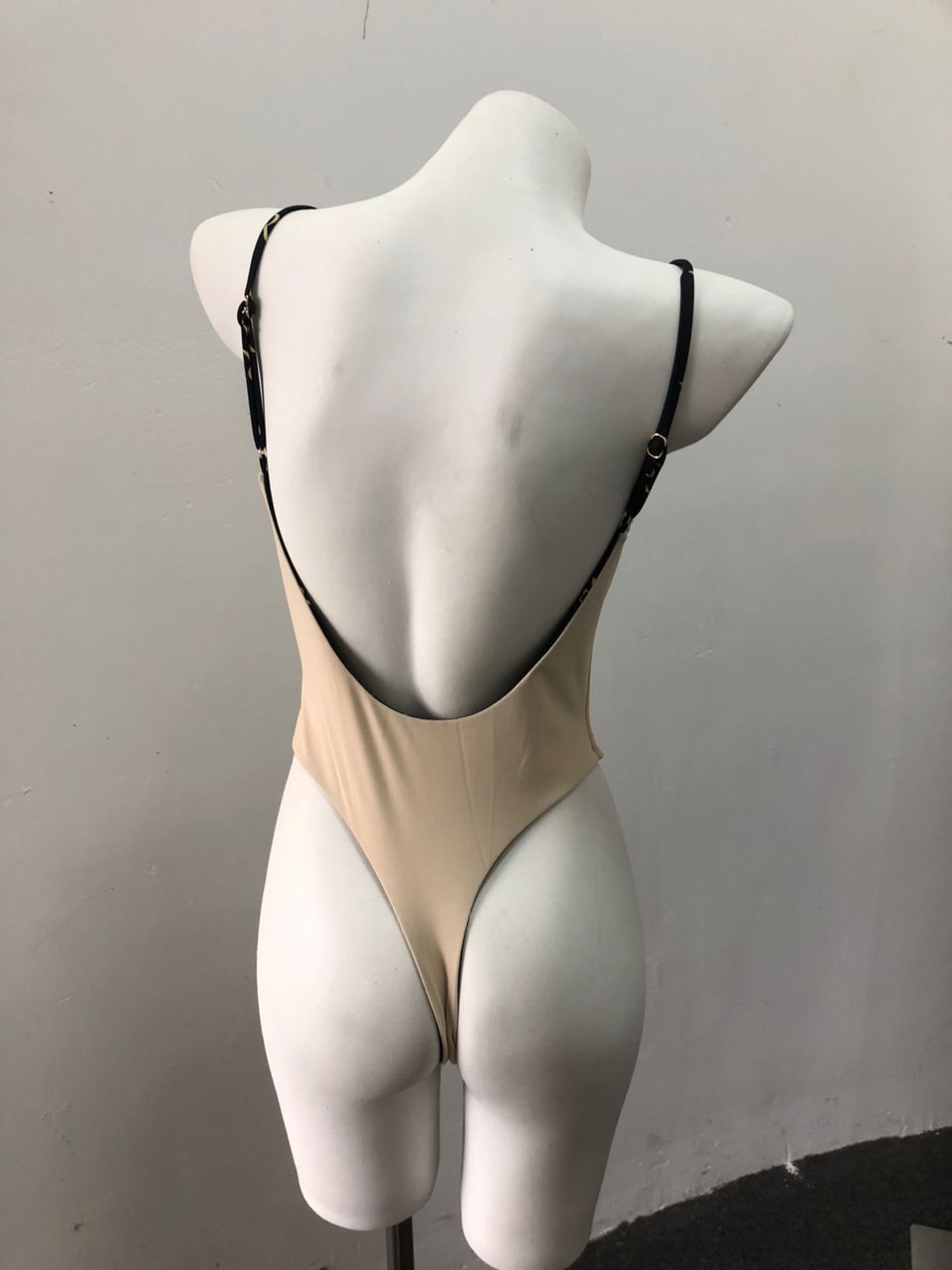 Nude backless swimsuit with black strap details on mannequin.