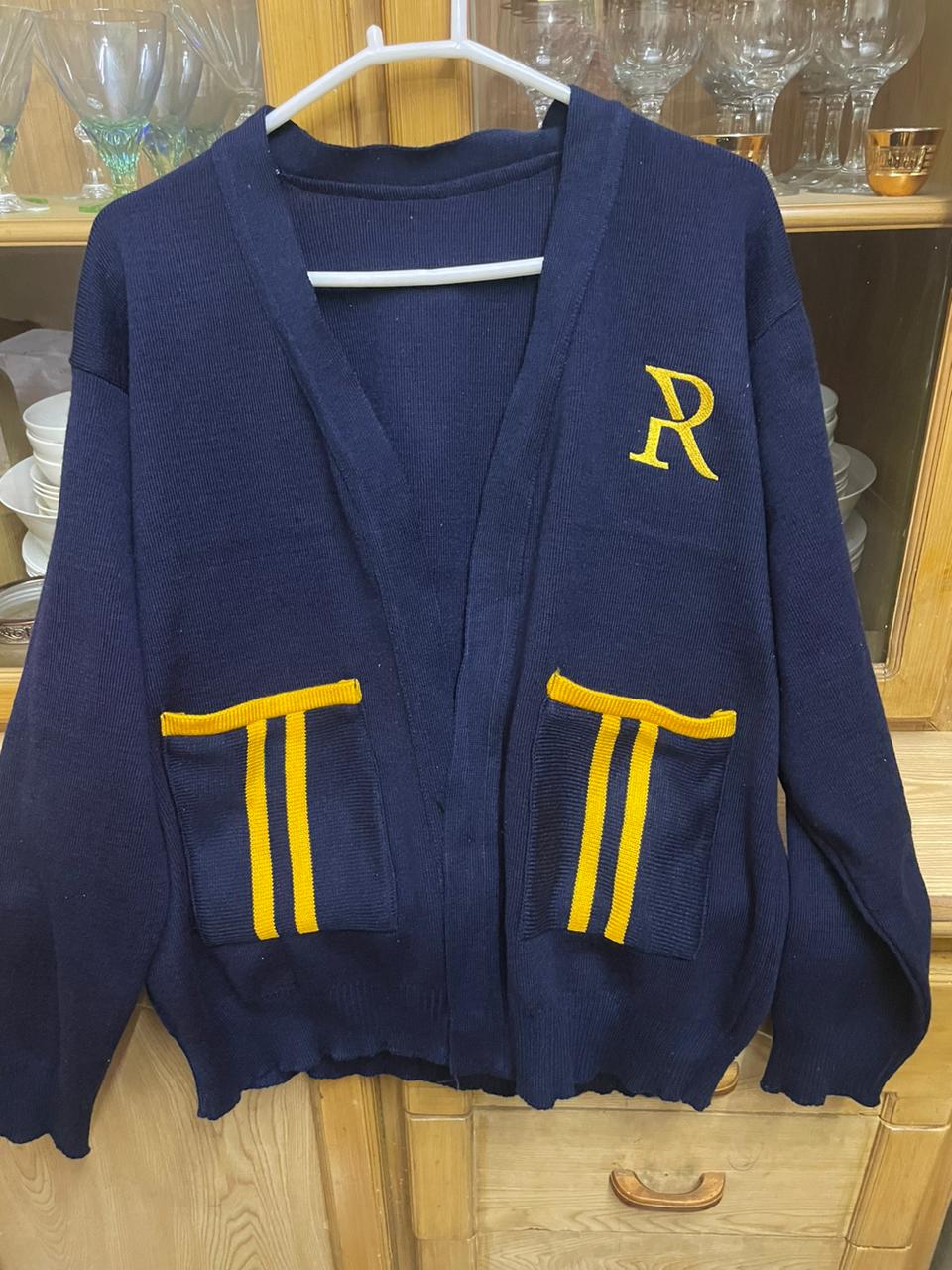 Navy blue varsity-style cardigan with yellow letter "R" and pockets with yellow stripes, displayed on a clothes hanger.