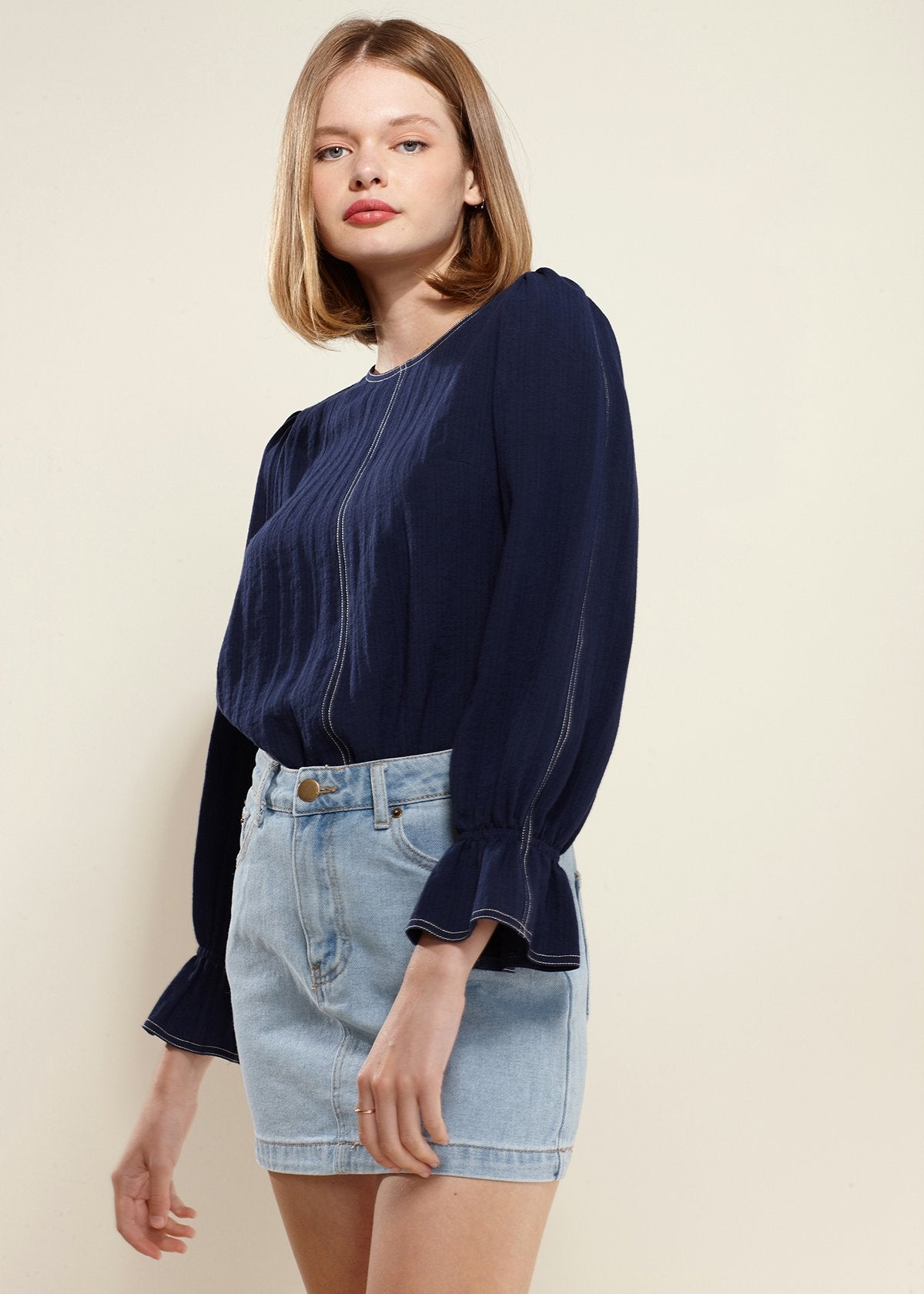 Navy blue puff shoulder top with bell cuff sleeves, worn with denim shorts, displayed on female model with blonde hair.