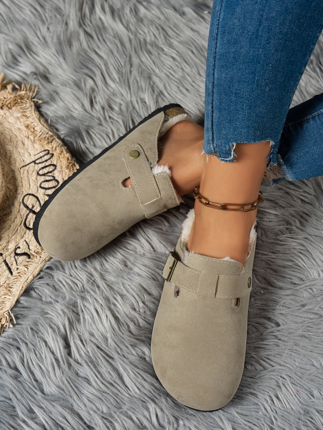 Cozy suede round-toe slippers in a neutral hue, resting on a plush grey faux fur rug.