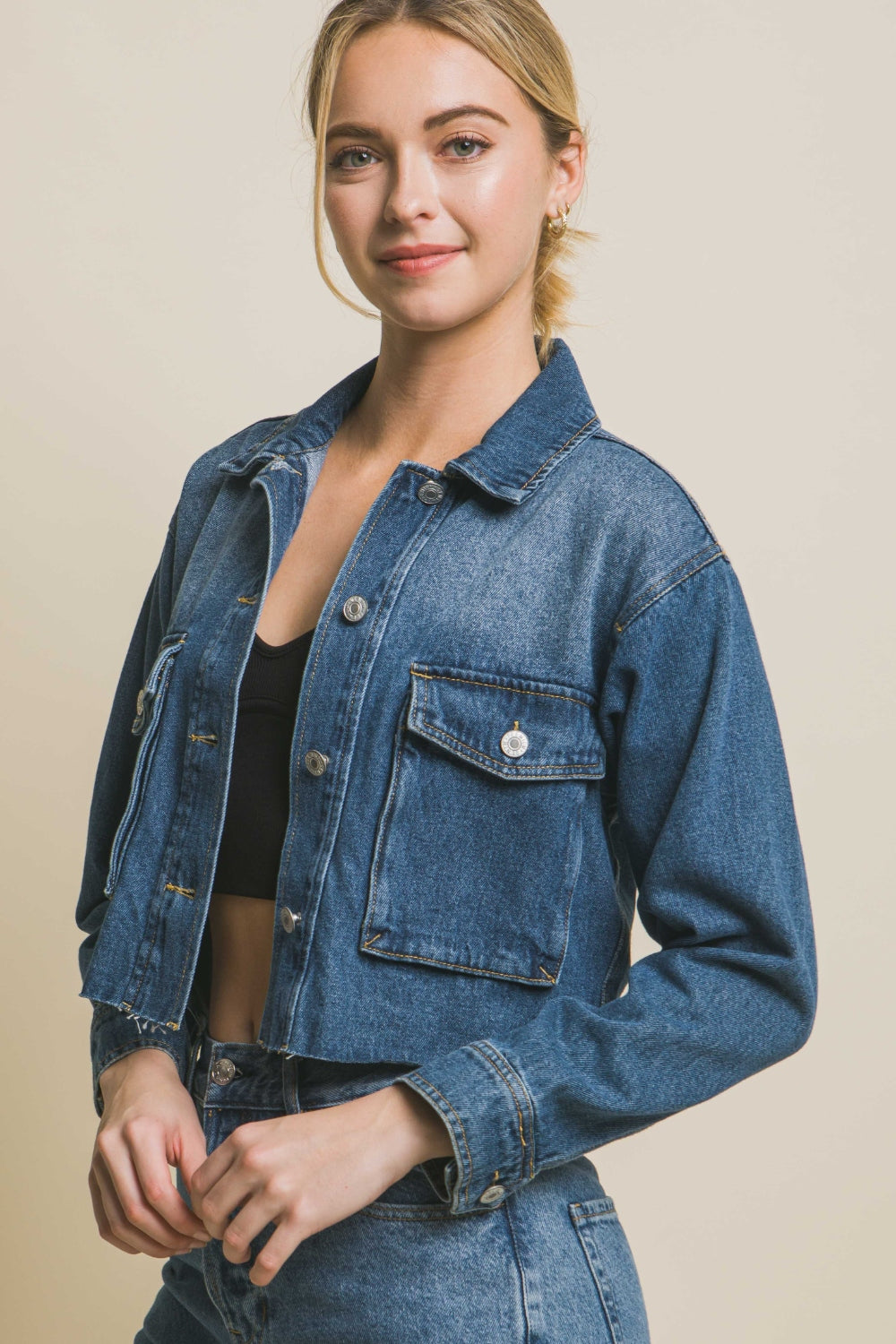 Stylish denim jacket with raw hem and button-up design, worn by a smiling woman with blonde hair against a neutral background.