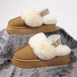 Plush beige platform slippers with fuzzy white straps and logo detailing, displayed on a gray fluffy surface.