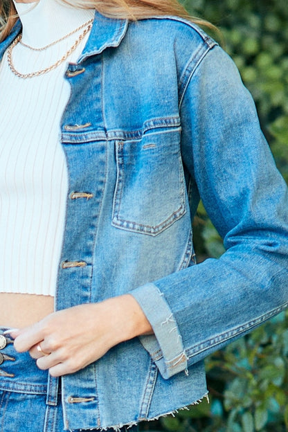 Denim button-up jacket with raw hem detail, styled with casual accessories on a blurred nature background