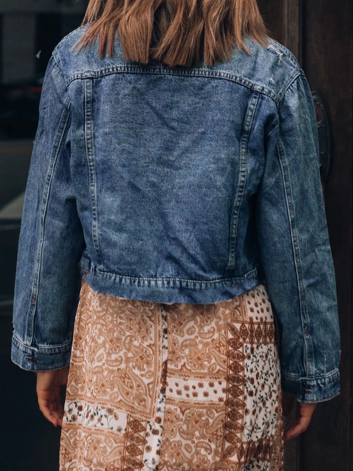 Distressed denim jacket with button-up collar, worn over a patterned skirt, showcasing a stylish casual outfit.