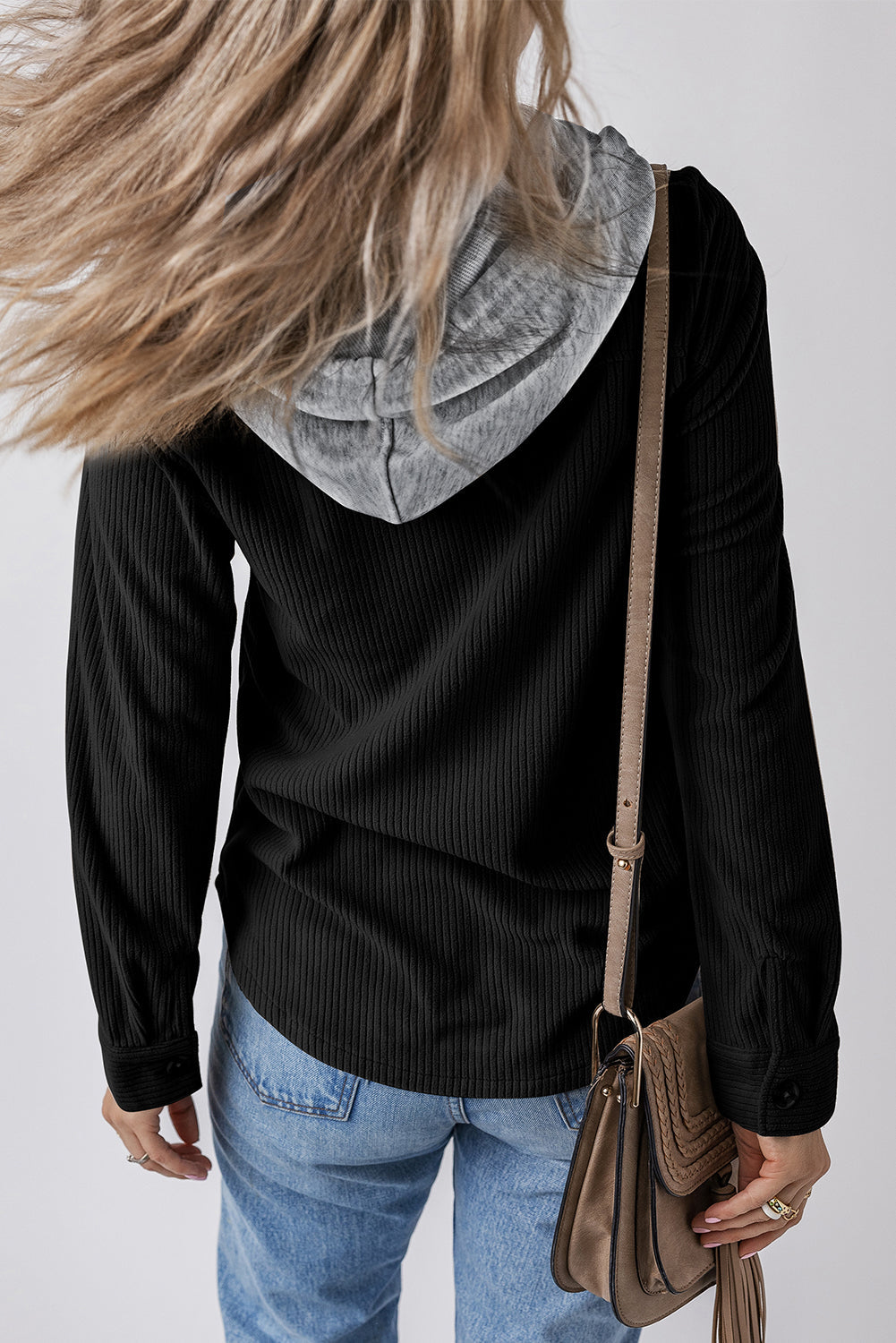 Casual hooded black corduroy jacket with drawstring waist and pockets, paired with denim jeans and a leather shoulder bag.