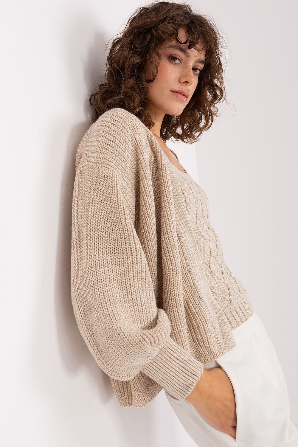 Cozy cable-knit ivory sweater with voluminous sleeves, showcasing a model's curled brown hair and stylish fashion sense.