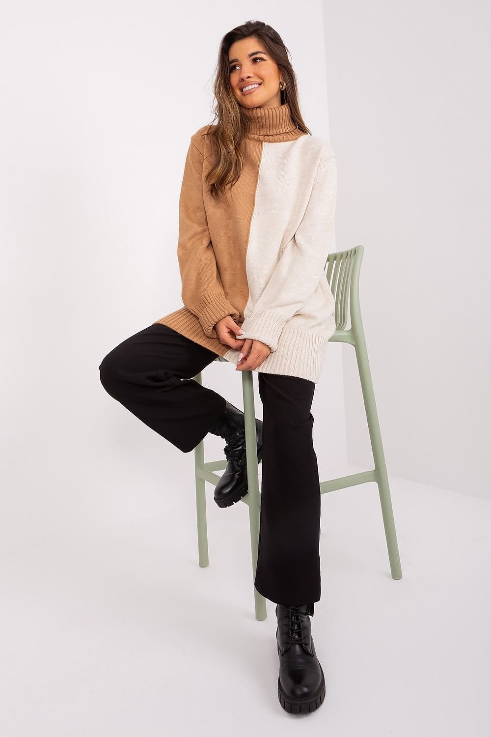 Cozy turtleneck sweater in neutral tones, worn by a smiling young woman seated on a green chair against a white background.