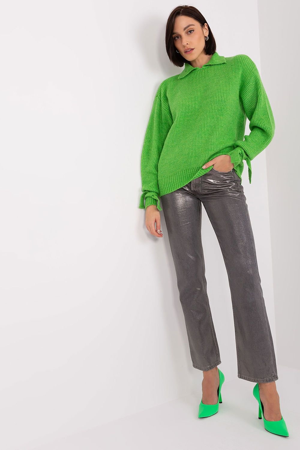 Bright green oversized knit jumper by Badu showcased on a female model with dark hair, wearing grey flared trousers and green high heels.