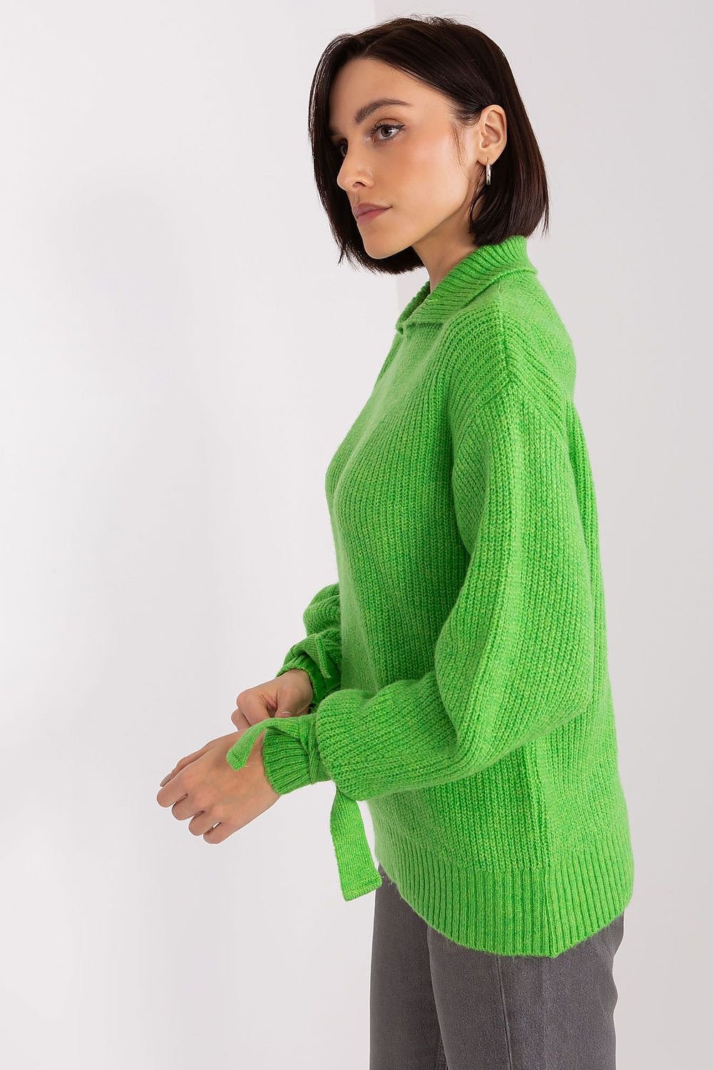 Bright green knitted jumper with long sleeves and a ribbed texture, worn by a young woman in a studio setting.