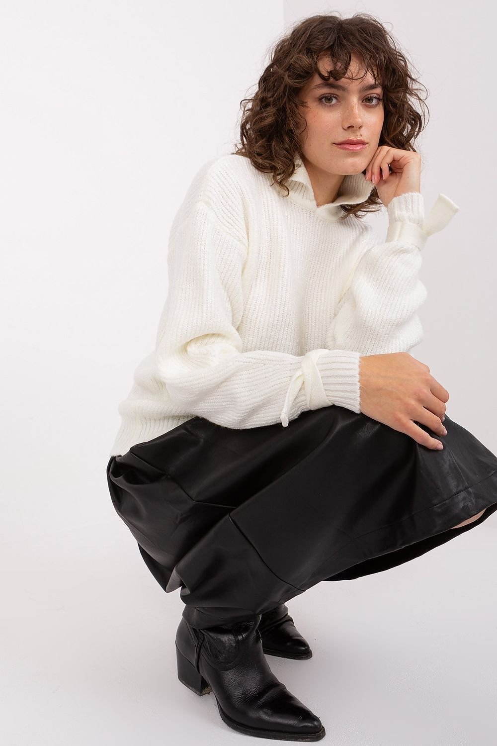 Cozy ivory sweater with a textured pattern, worn by a young woman with curly hair, seated and posing against a plain white background.