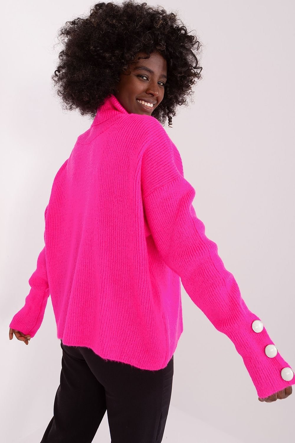 Bright neon pink ribbed turtleneck sweater with flared cuffs modeled by a smiling woman with curly dark hair