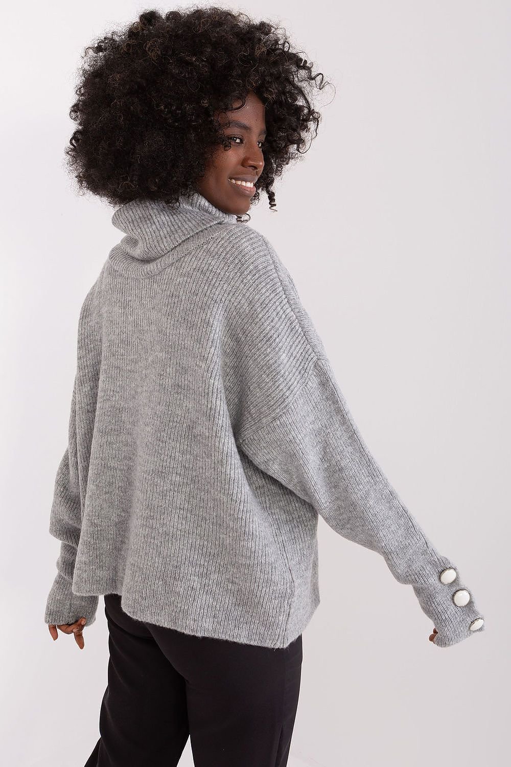 Cozy gray turtleneck sweater with cuffed sleeves, modeled by a smiling woman with curly dark hair against a plain background.