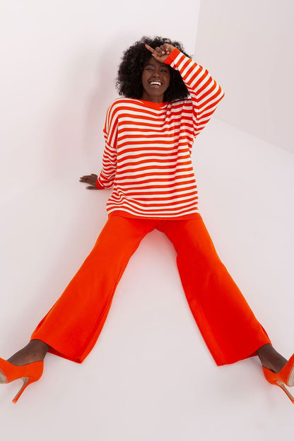 Red and white striped top and orange flared pants worn by a smiling woman with curly hair in front of a white background.