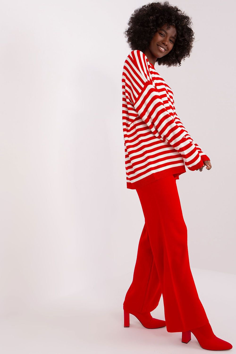 Vibrant striped top and flared crimson pants worn by a smiling woman with curly hair, posing against a white background.