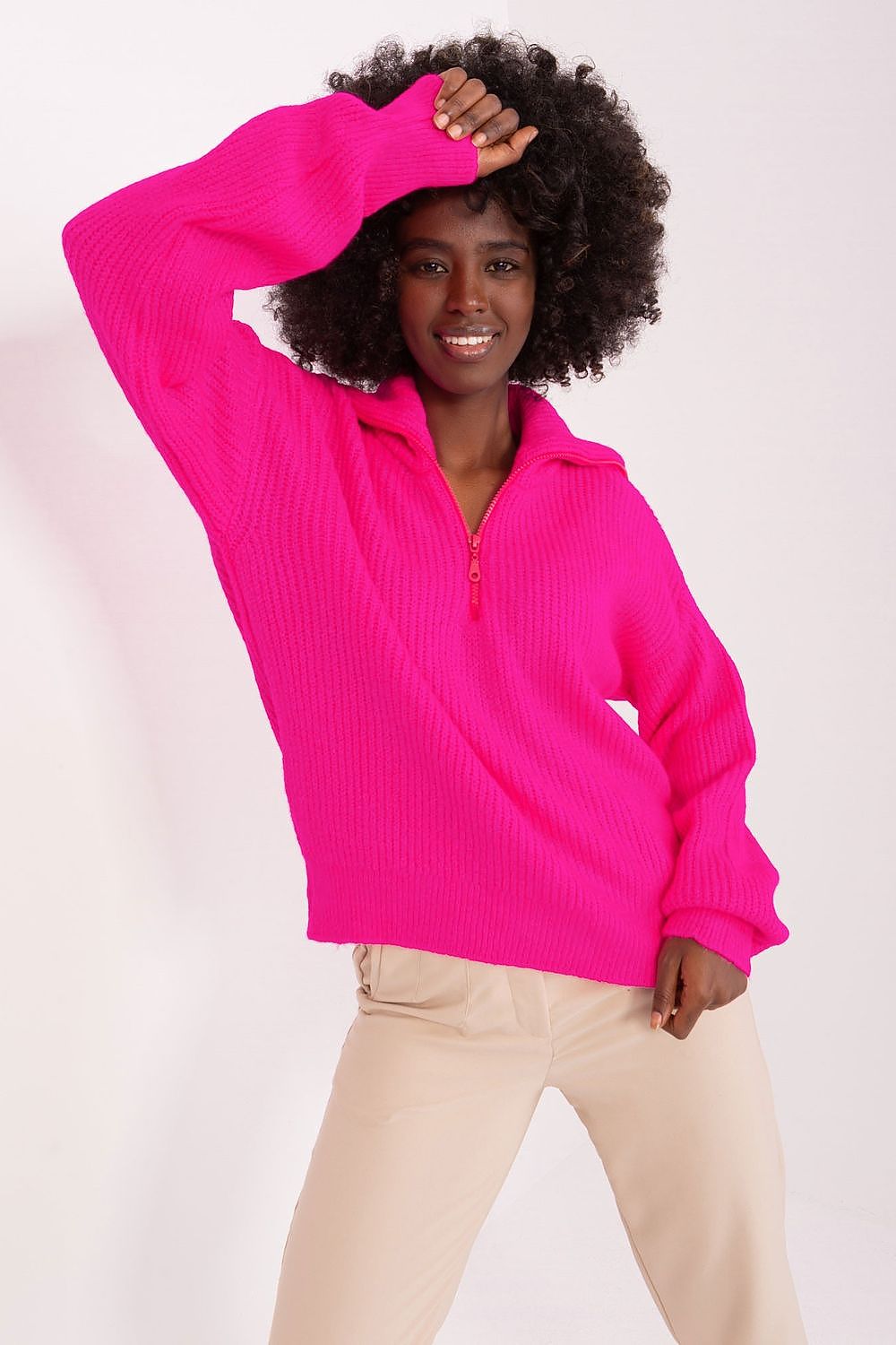 Bold and vibrant pink turtleneck sweater showcased on a smiling young woman with curly dark hair against a white background.