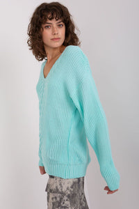 Turquoise knit sweater worn by a woman with curly dark hair against a white background