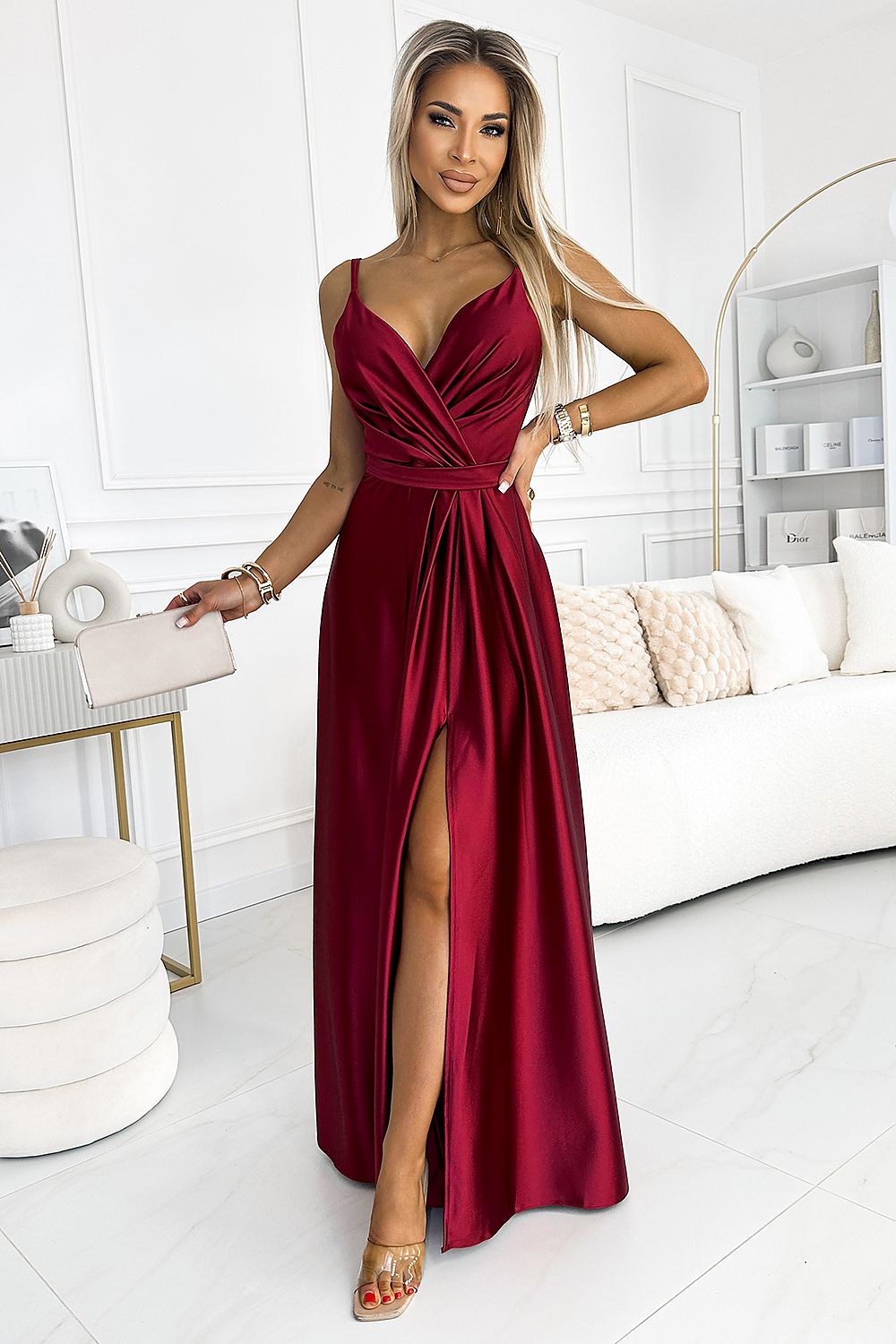 Elegant burgundy evening gown with deep V-neckline and thigh-high slit, complemented by model's styling in modern, minimalist setting.