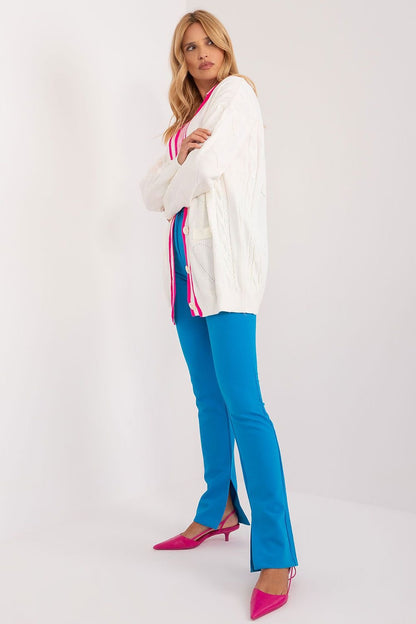 Stylish woman in bright colored outfit, featuring a white cardigan, pink and blue striped top, and bold blue trousers with vibrant pink heels.