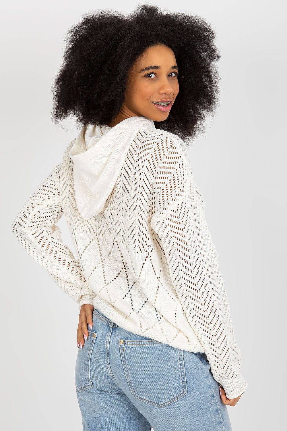 Cozy crocheted ivory sweater with intricate patterns, worn by a smiling woman with curly dark hair.