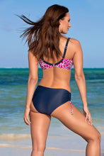 Load image into Gallery viewer, Vibrant swimsuit featuring floral print top and solid navy bottoms, worn by a woman with flowing brown hair on a sunny beach.