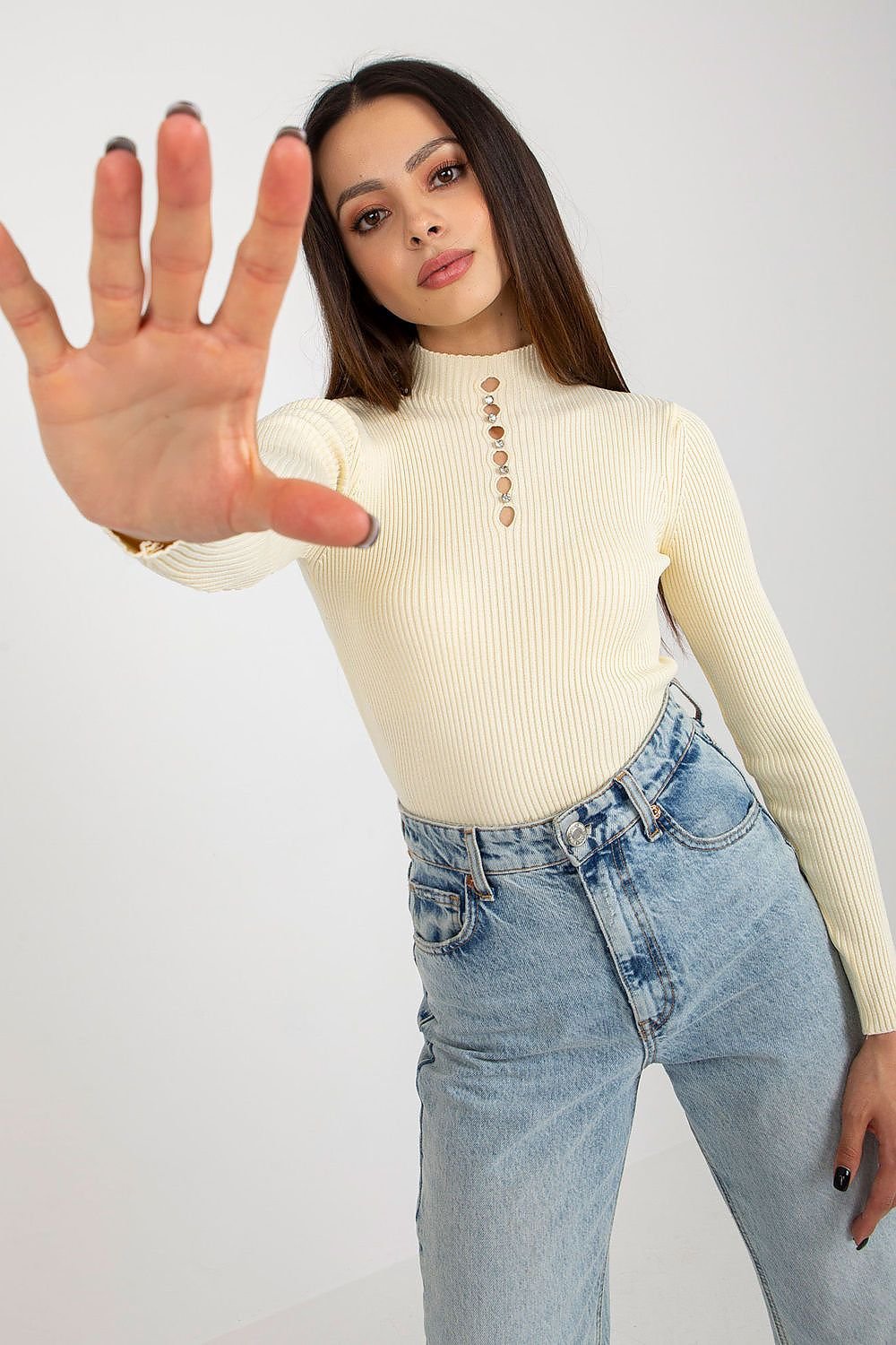 Vibrant retro-inspired ivory ribbed knit top featuring a high neckline and button detailing, styled with high-waisted light wash denim jeans.