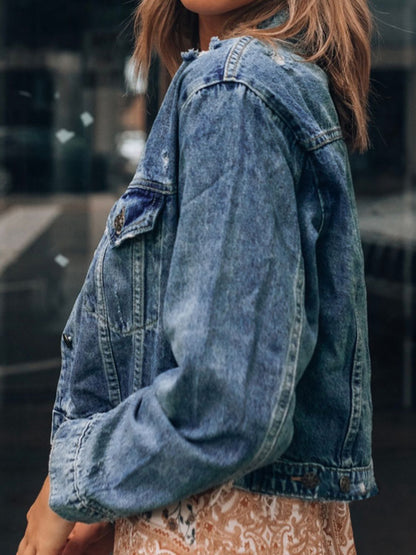 Distressed denim jacket with button up collared neck, worn over printed dress in rustic setting.