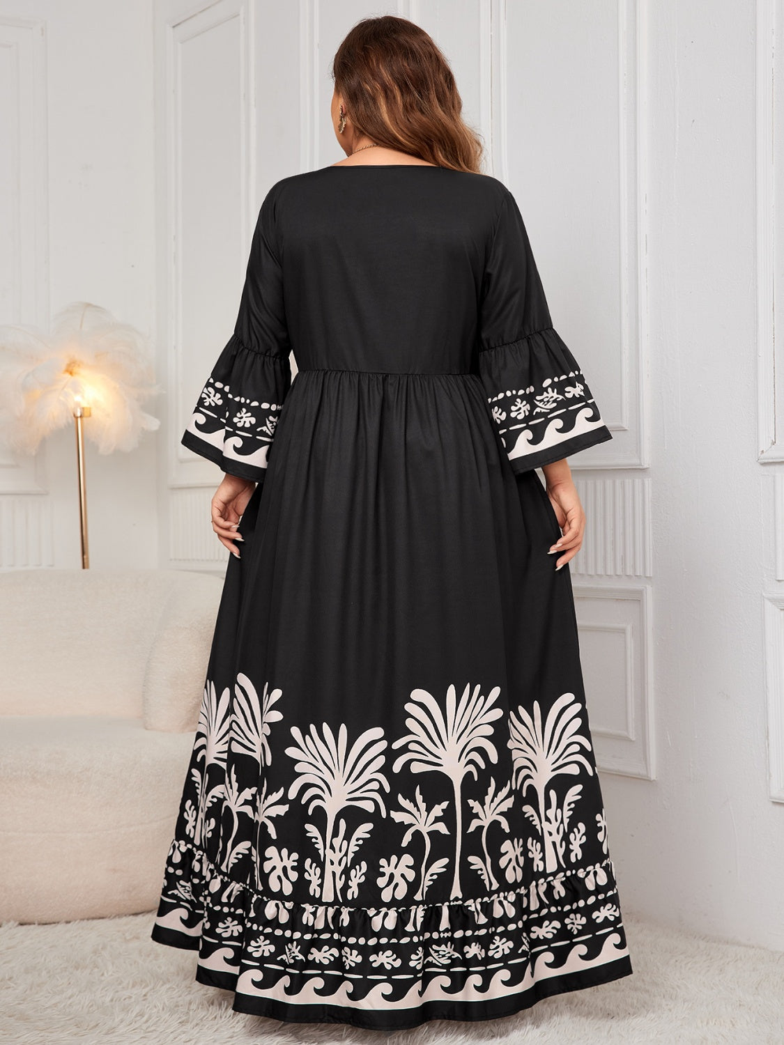 Elegant floral embroidered black maxi dress with ruffled sleeves, worn by a woman standing in an interior setting with a lamp.